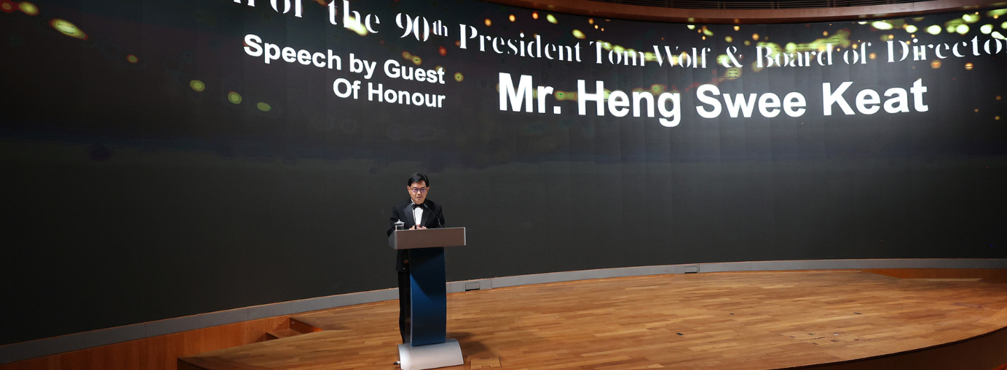 Man at podium, "Mr. Heng Swee Keat" on screen, stage is wood.
